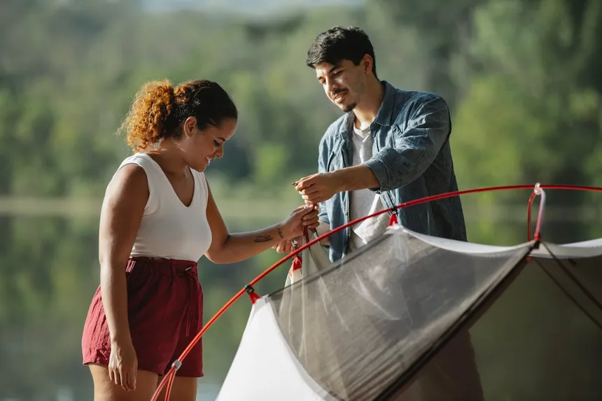 Couple setting up camping tent near a lake, perfect scenario for portable power station use