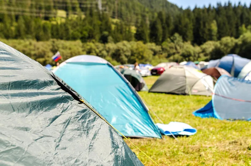 Camping tents set up at an outdoor campground with pine forest and mountains in the background