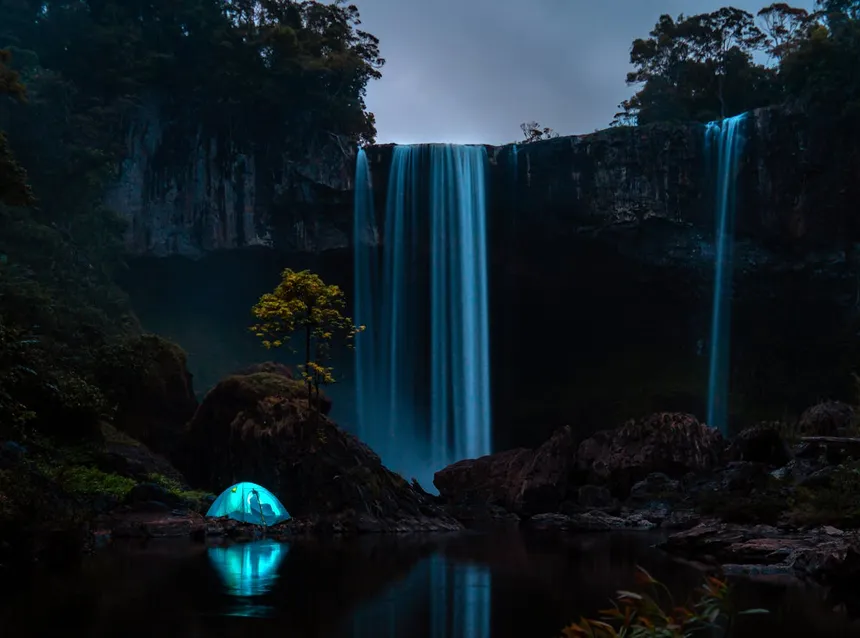 Illuminated camping tent at night by a waterfall, showing remote camping where a power station keeps CPAP running