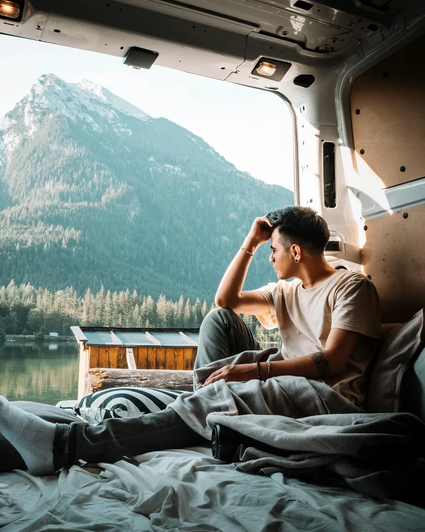 Man sitting in converted campervan looking out at mountain lake scenery, representing the van life lifestyle that requires portable power